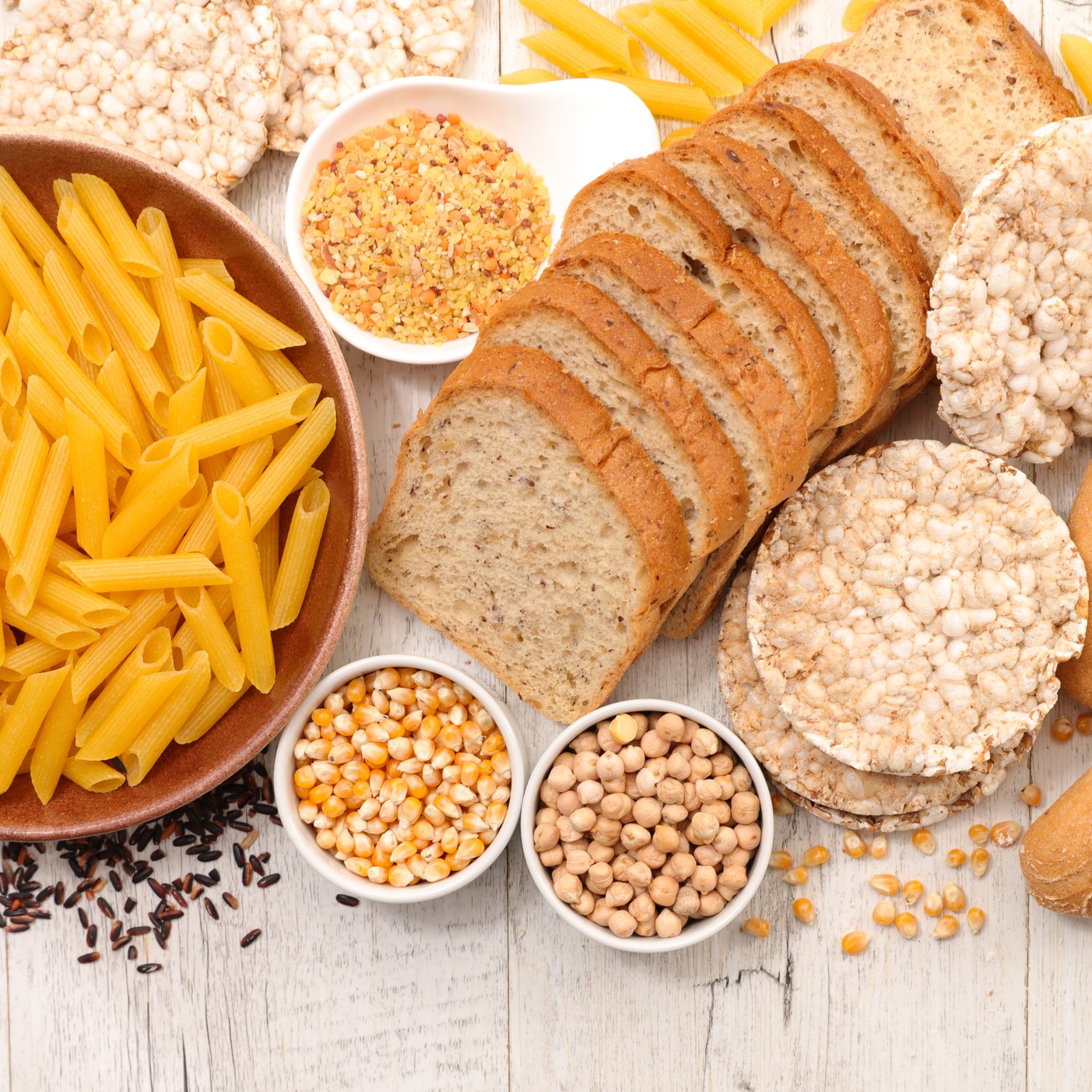 Products containing gluten on wooden table, including pasta, bread, and rice cakes.