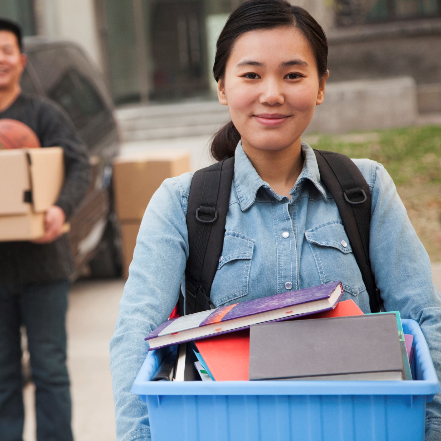 Student in front of a dorm, moving in and carrying a box of books