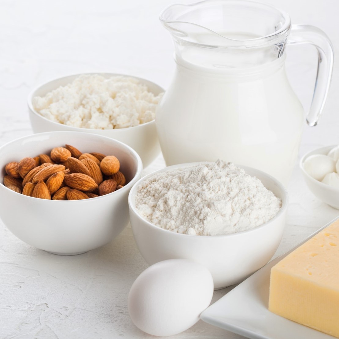 Glass jar of milk, bowl of cottage cheese, baking flour, almond, and eggs on table.